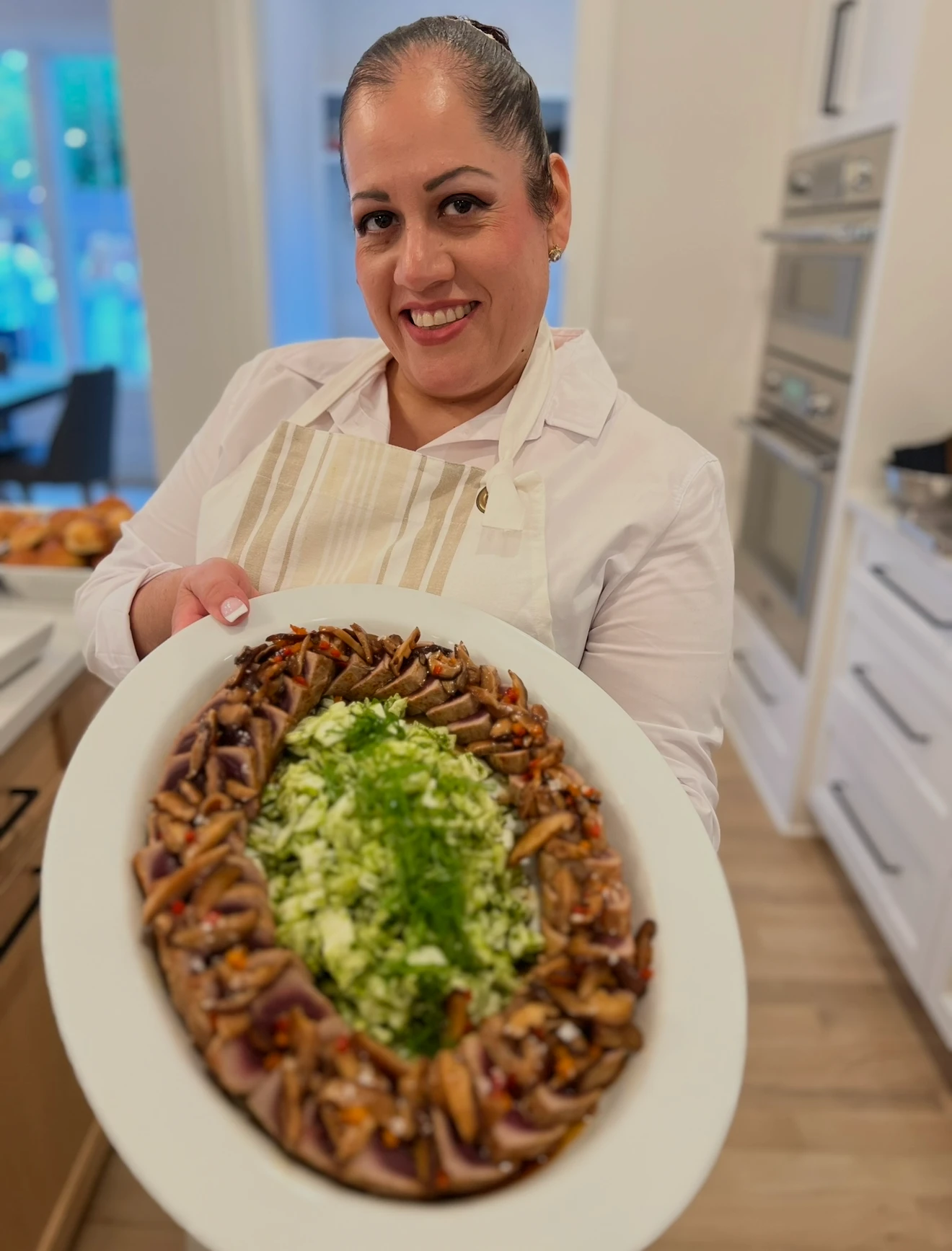 Alba Rocío Fernández smiling in a kitchen, holding a large platter she prepared